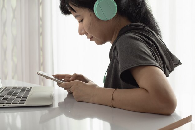 Mulher usando fones de ouvido, usando smartphone com laptop e ficar em casa para auto-quarentena