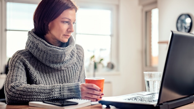 Mulher usando laptop e bebendo café