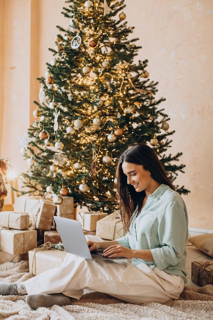 Mulher usando laptop e sentada perto da árvore de Natal