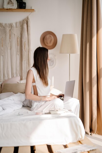 Mulher usando laptop enquanto está sentada na cama em casa
