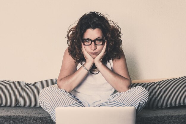 Foto mulher usando laptop enquanto está sentada no sofá em casa