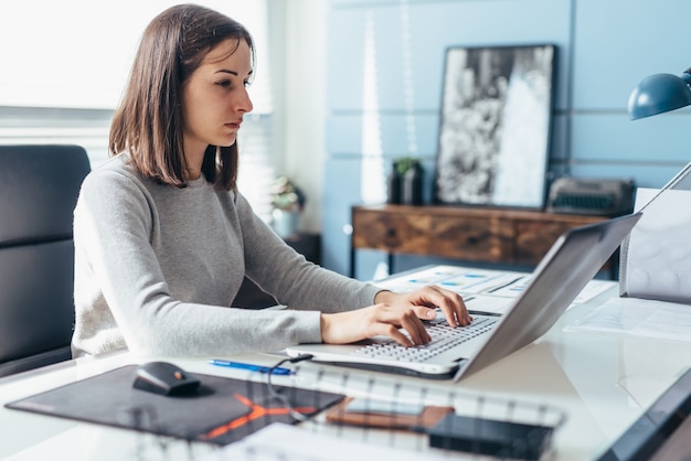 Mulher usando laptop enquanto está sentado em sua mesa. Mulher de negócios no escritório trabalhando no laptop.