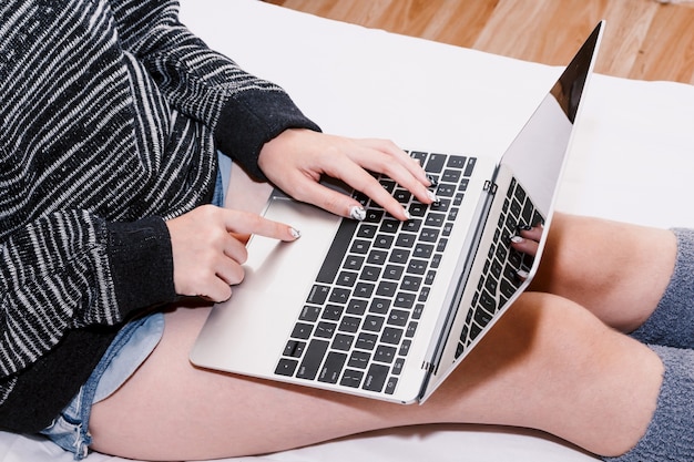 Mulher usando laptop na cama branca em casa