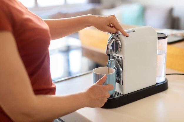 Mulher usando máquina de café expresso na cozinha derramando café na xícara