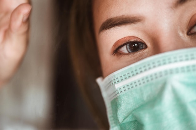 Mulher usando máscara de proteção na janela espera que a situação epidêmica melhore logo em casa. Coronavirus, covid-19, Trabalho de casa (WFH), Distanciamento social, Quarentena, Conceito de prevenção de infecção.