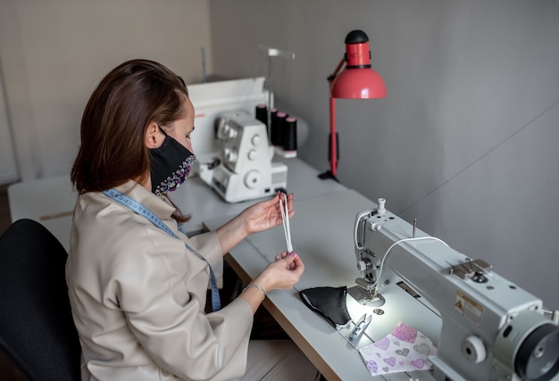 mulher usando máscara e costura máscaras em uma máquina de costura para se proteger contra covid-19. Máscara protetora caseira contra o vírus covid19.