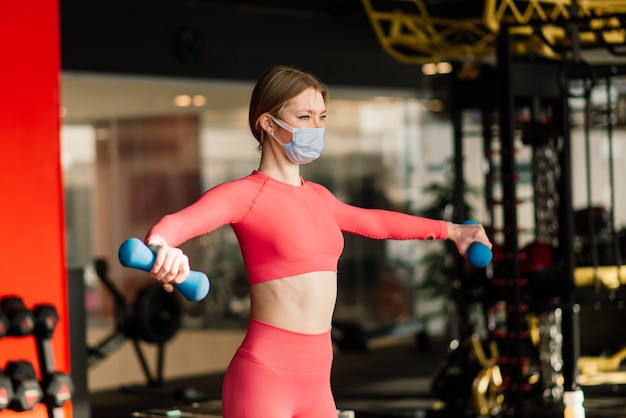 Mulher usando máscara facial treino de exercícios na academia durante o vírus corona pandérmico, cobiçoso