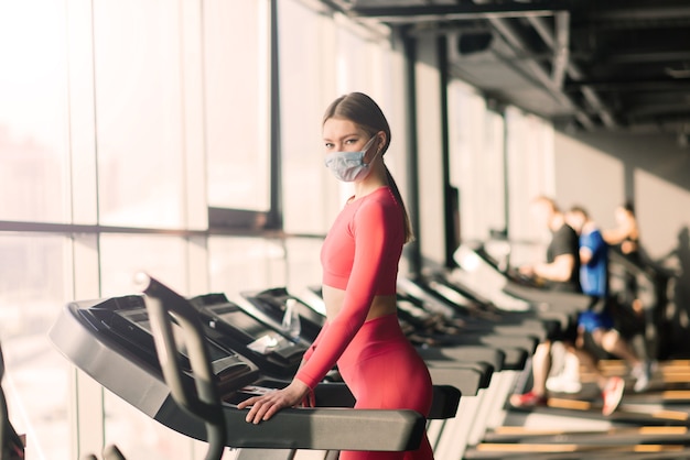 Mulher usando máscara facial treino de exercícios na academia durante o vírus corona pandérmico, cobiçoso