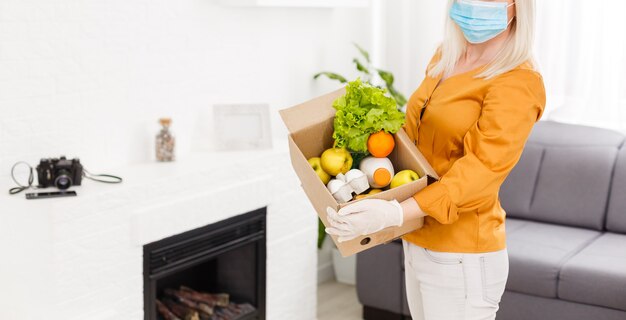 mulher usando máscara médica Desmonta os sacos de comida em casa na cozinha. quarentena. conceito de saúde. Vírus Corona. pedido de produtos online. Entrega de produtos em casa