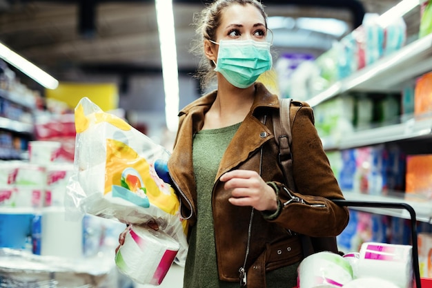 Mulher usando máscara protetora ao comprar estoque de papel higiênico no supermercado durante epidemia de vírus