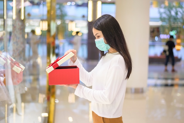 Mulher usando máscara protetora segurando uma caixa de presente em um shopping