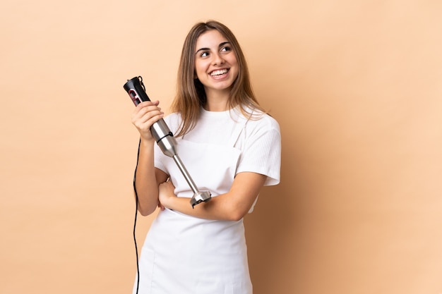 Mulher usando o liquidificador sobre isolado olhando para cima enquanto sorrindo