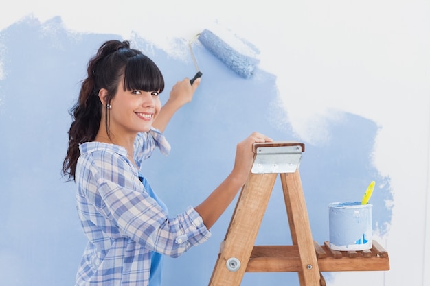 Mulher usando o rolo de pintura para pintar a parede e sorrindo para a câmera