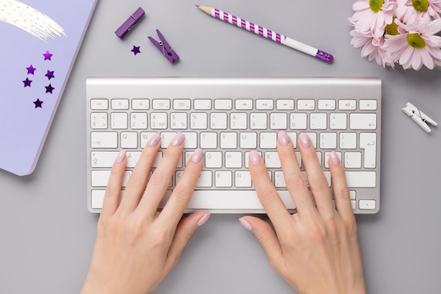 Mulher usando o teclado na mesa cinza com caderno, papelaria e flores. Conceito de negócio para mulheres