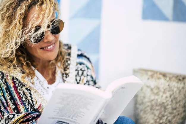 Mulher usando óculos de sol lendo um livro enquanto está sentada ao ar livre