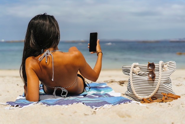 Mulher usando seu smartphone deitado na areia da praia.