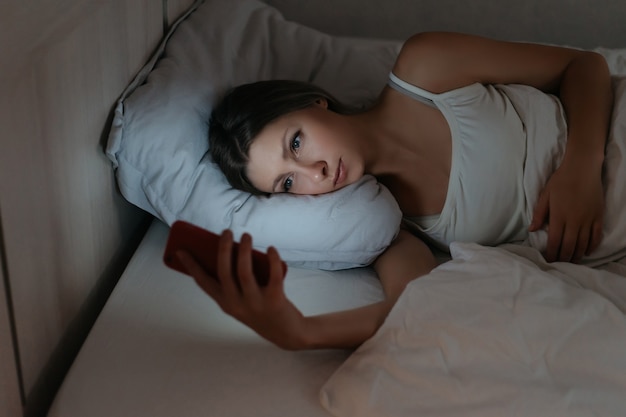 Mulher usando seu smartphone na cama à noite, em vez de dormir