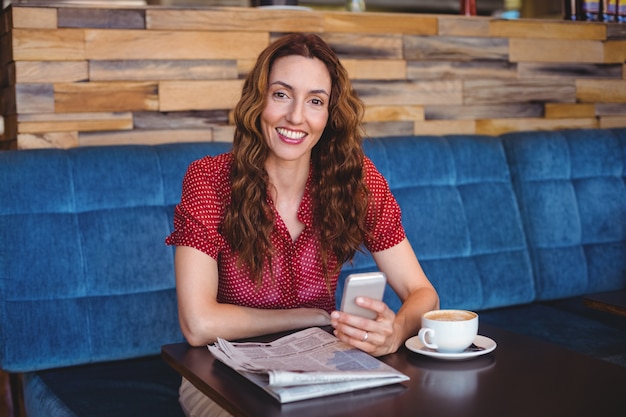 Mulher usando seu telefone celular e segurando xícara de café