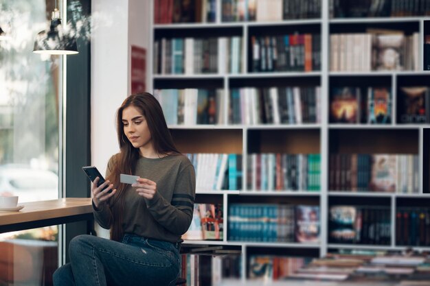 Mulher usando smartphone e cartão de crédito para compras online em um café