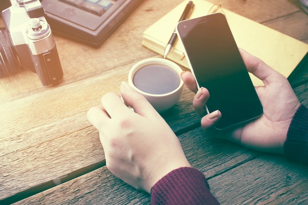 Mulher usando smartphone e xícara de café na mesa de trabalho