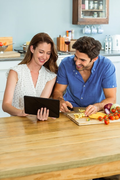 Mulher usando tablet digital e homem cortar legumes