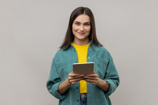 Mulher usando tablet para verificar redes sociais olhando para câmera com expressão positiva