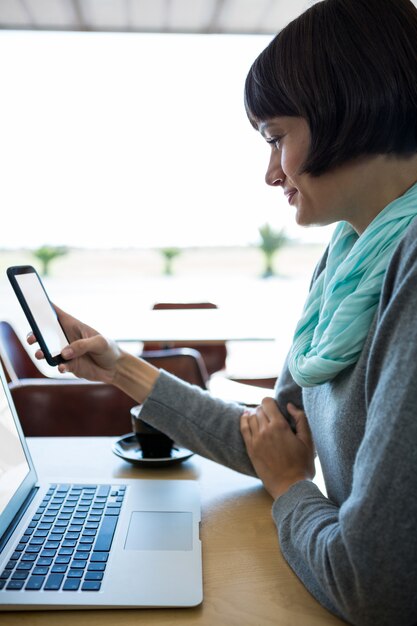 Mulher usando telefone celular com o laptop na mesa