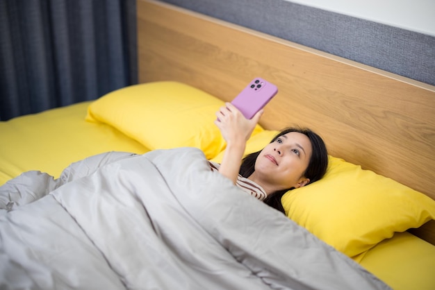 Mulher usando telefone celular e deitada na cama