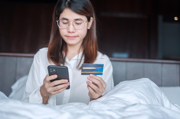 Mulher usando telefone celular inteligente e cartão de crédito para compras on-line enquanto faz o pedido na cama de manhã em casa. tecnologia, comércio eletrônico, pagamento on-line de banco digital e conceito de vida em apartamento