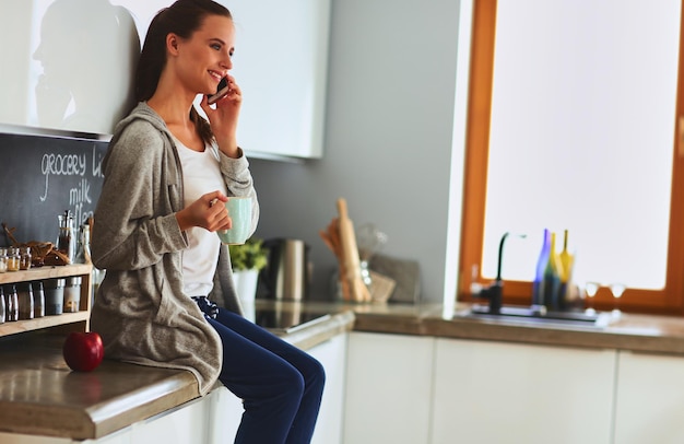 Mulher usando telefone celular sentado na cozinha moderna