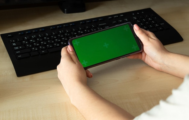 Mulher usando telefone inteligente móvel com tela verde na mesa com computador e teclado