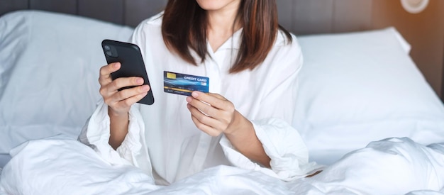 Mulher usando telefone inteligente móvel e cartão de crédito para compras on-line enquanto faz o pedido na cama de manhã em casa tecnologia ecommerce banco digital pagamento on-line e conceito de vida em apartamento