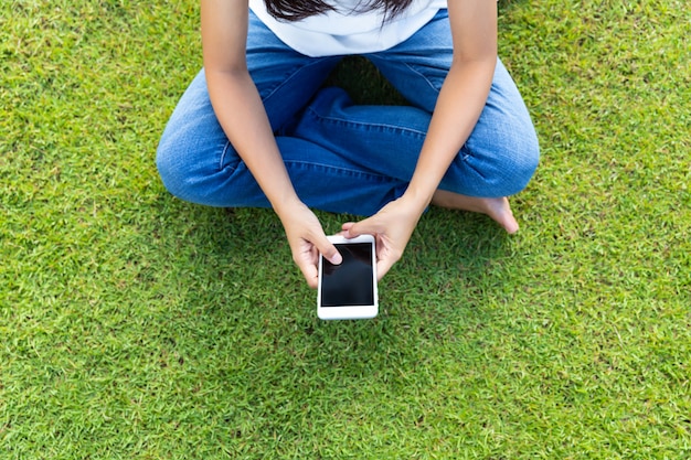 Mulher usando telefone móvel esperto na grama para relaxar com as mídias sociais