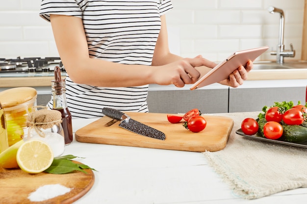 Mulher usando um computador tablet para cozinhar na cozinha dela