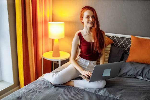 Mulher usando um laptop à noite sentada em um sofá no quarto ruim em casa