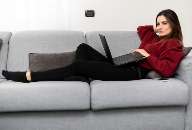 Mulher usando um laptop enquanto relaxa no sofá