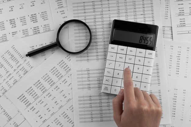 Foto mulher usando uma calculadora com lupa e demonstrativo financeiro sobre a mesa