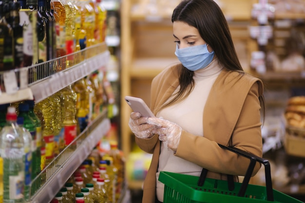 Mulher usando uma máscara protetora e luvas no supermercado. Compras durante a quarentena pandêmica