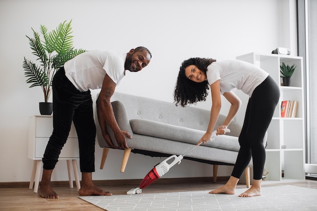 Mulher usando vácuo para limpar debaixo do sofá aquele homem levantando