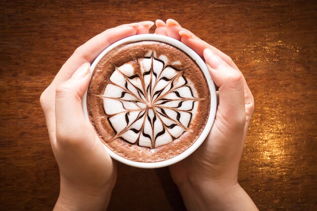 Foto mulher usar duas mãos segurando a xícara de café. café com latte art. vista superior com vigne escuro