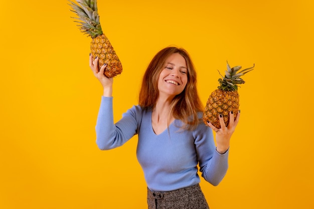 Mulher vegetariana com um abacaxi em óculos de sol dançando e feliz vida saudável fundo amarelo