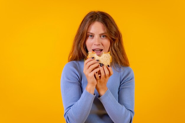 Mulher vegetariana comendo um sanduíche em uma comida vegetariana saudável de fundo amarelo