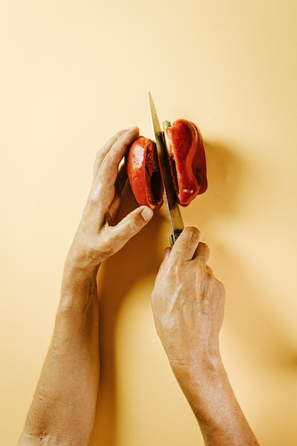 Mulher velha com as mãos cortando uma pimenta