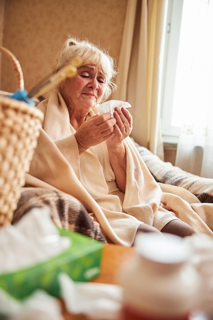 Mulher velha infeliz com gripe usando lenço