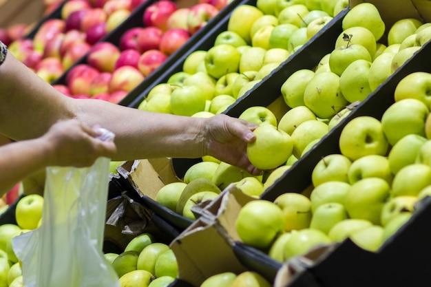 Mulher velha selecionando maçãs frescas no departamento de produtos de mercearia e colocando-as em um saco plástico.