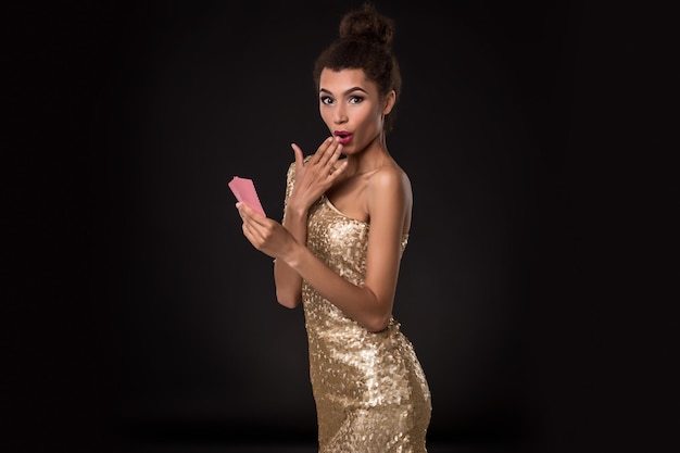 Mulher vencedora - jovem mulher em um elegante vestido de ouro segurando duas cartas, um pôquer de combinação de cartas de ases. estúdio filmado em fundo preto. emoções