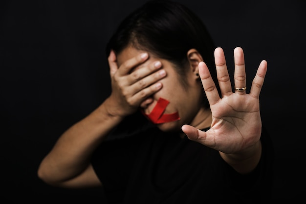 Mulher vendada envolvendo a boca com fita adesiva vermelha e mostrar sinal de mão para parar de abusar da violência