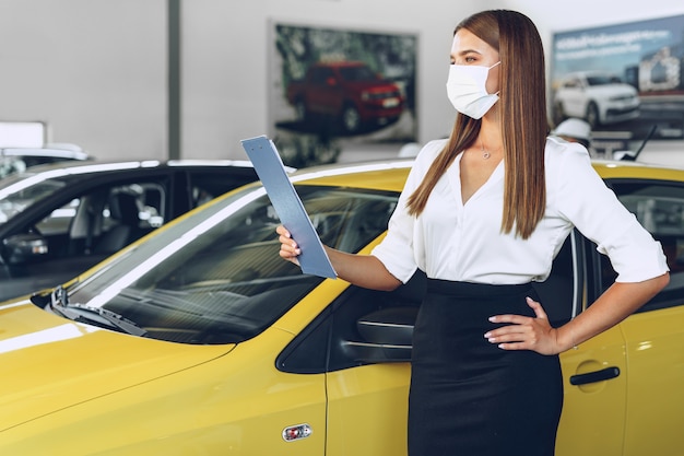 Mulher vendedora de carros perto de um carro novo usando máscara protetora