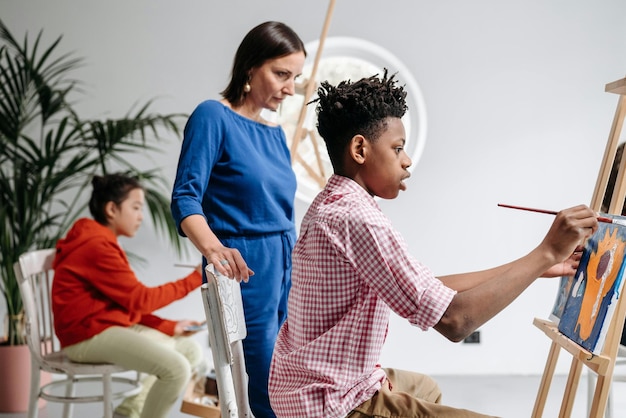 Foto mulher vendo crianças pintar durante uma aula de arte foto de estoque