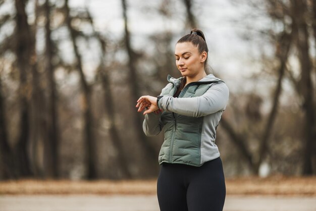 Foto mulher verificando o rastreador de fitness durante o treino ao ar livre no início da manhã